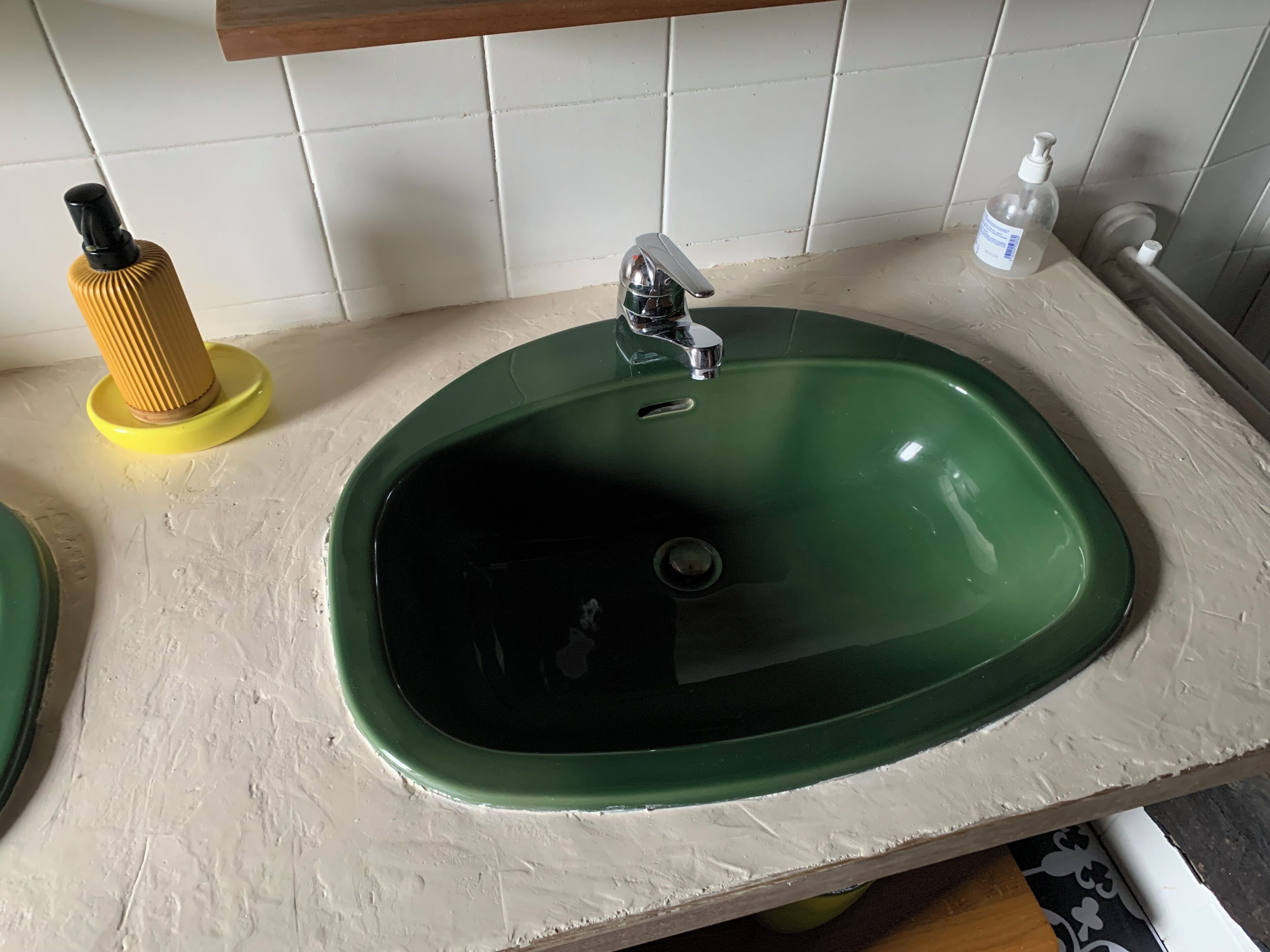 A green sink with a chrome faucet, a yellow soap dispenser, and a white bottle of hand sanitizer on the countertop.