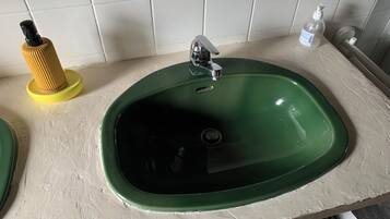 A green sink with a chrome faucet, a yellow soap dispenser, and a white bottle of hand sanitizer on the countertop.