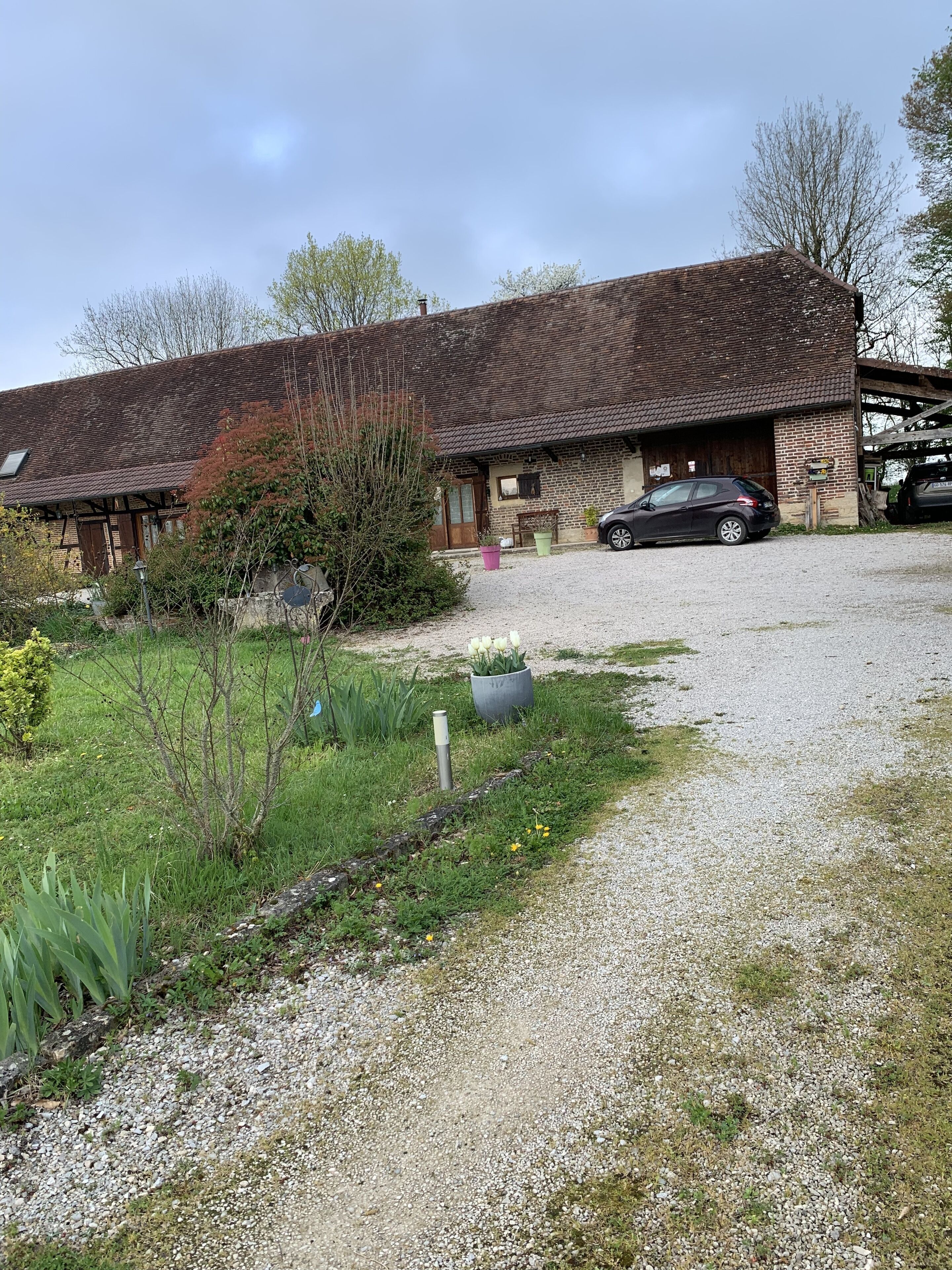 A rustic building with a gravel driveway, a parked car, and a garden area with various plants.