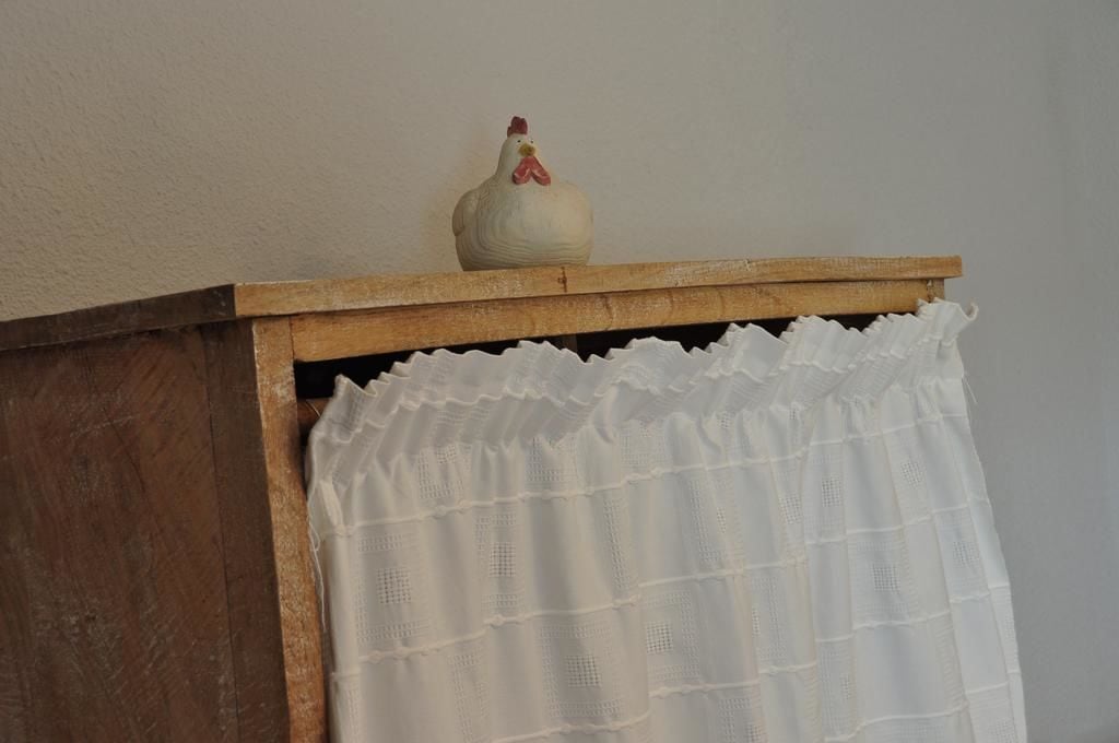 A wooden cabinet with a white curtain and a ceramic rooster on top.