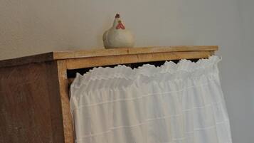 A wooden cabinet with a white curtain and a ceramic rooster on top.