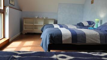 Une chambre avec deux lits, une commode en bois et une fenêtre laissant entrer la lumière naturelle.