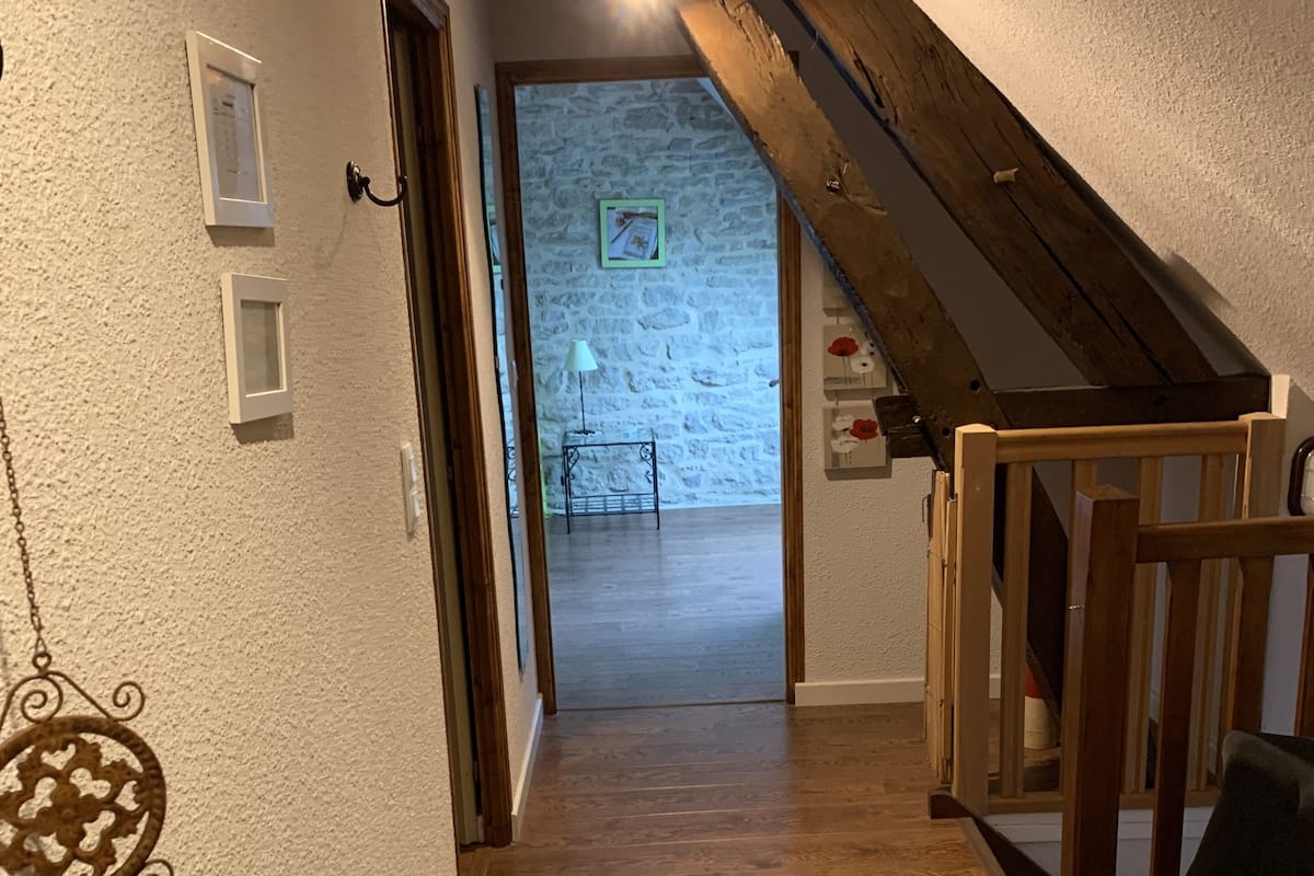 A hallway with wooden flooring, a staircase with a wooden handrail, and a wall-mounted light fixture.