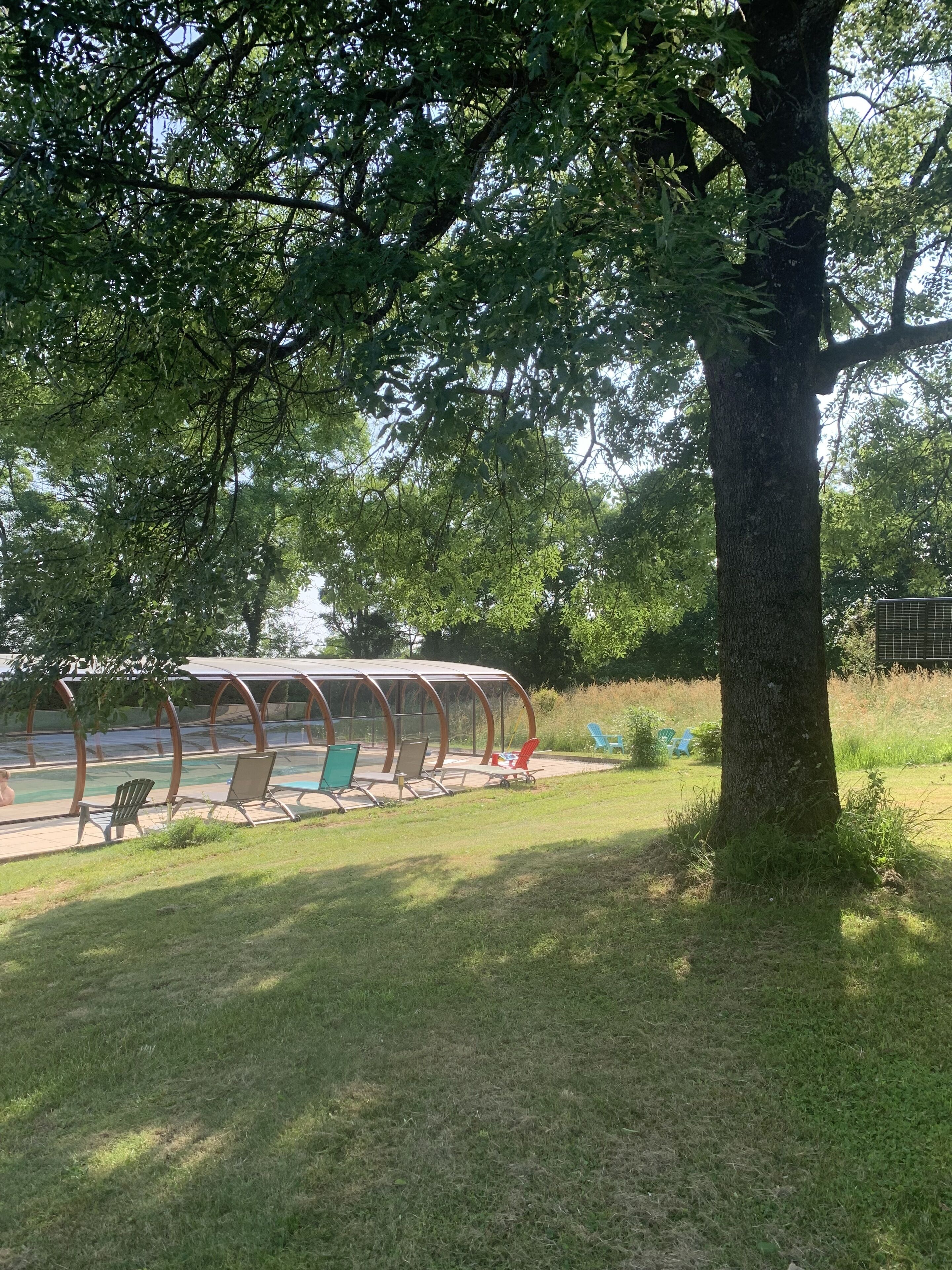 A covered outdoor seating area with chairs and a pool.