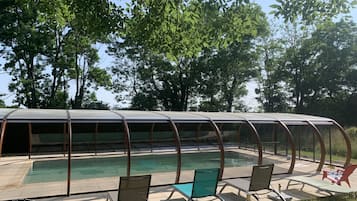 A covered swimming pool with lounge chairs and a glass enclosure.