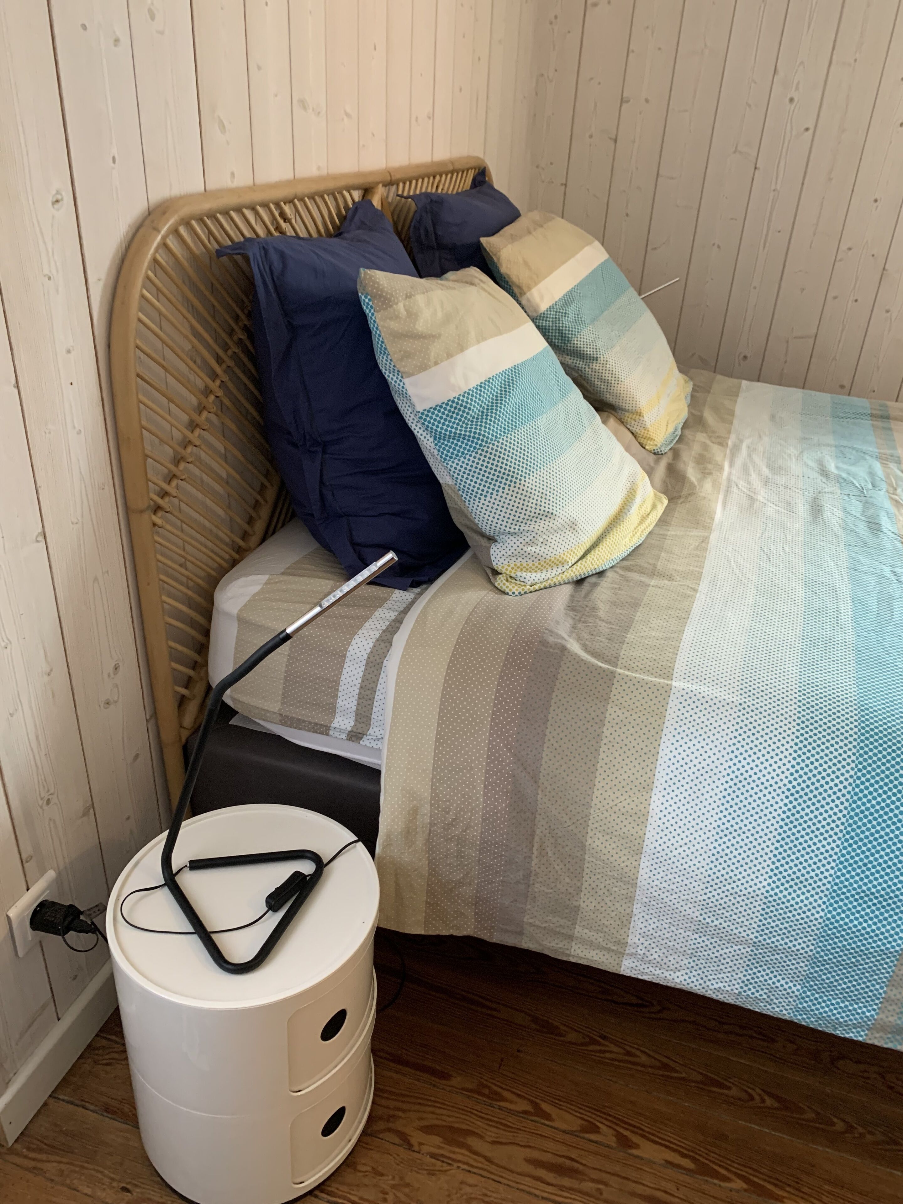 A bed with a striped blanket, two pillows, and a bedside table with a lamp.