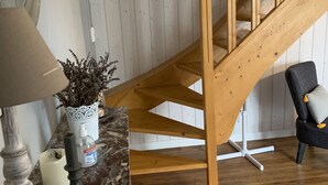 Una escalera de madera con barandal blanco, una planta en maceta, una lámpara y un sillón con cojín.
