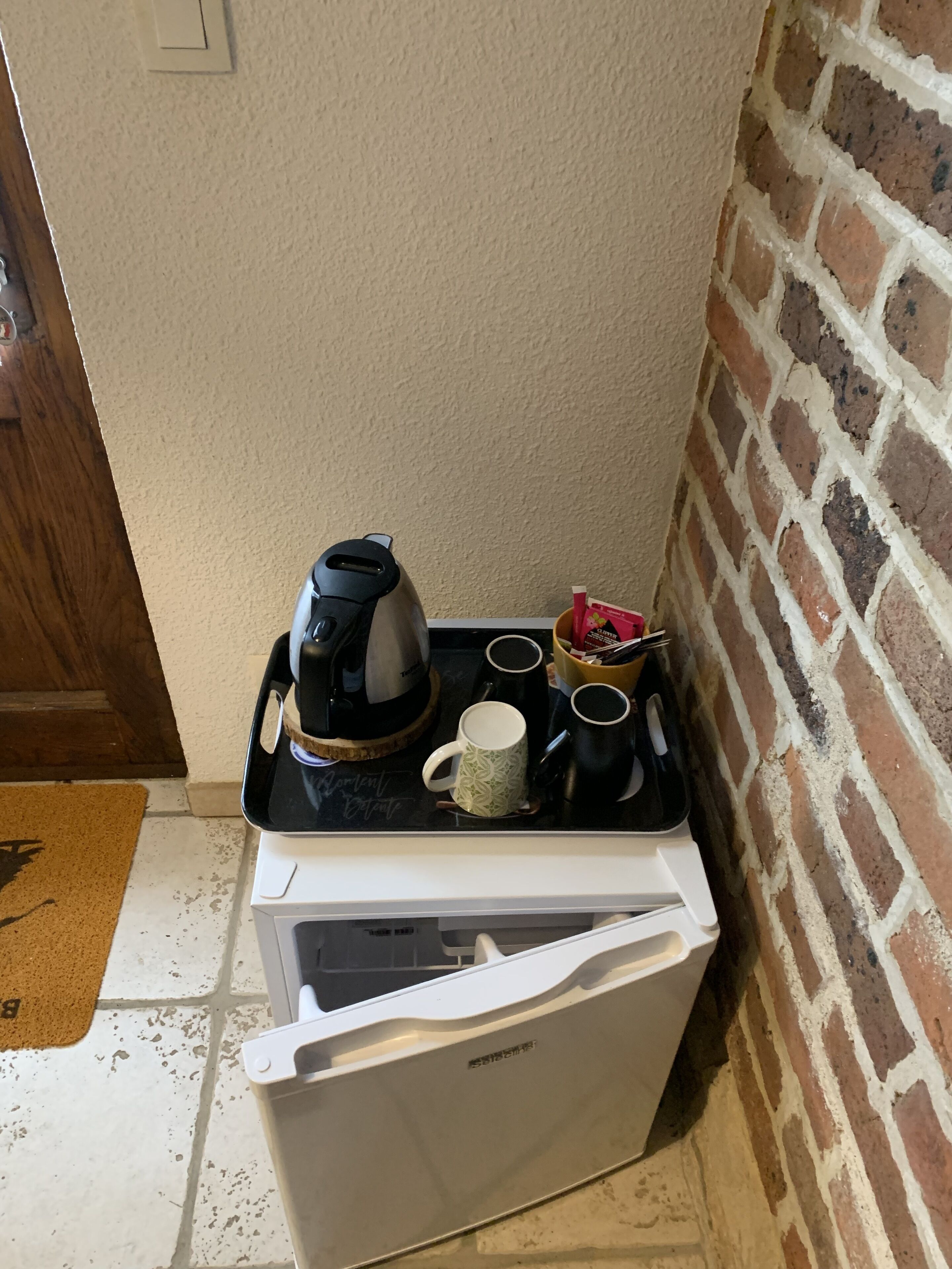 Una kitchenette compacta con cafetera, tazas y un refrigerador pequeño.