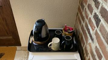Una kitchenette compacta con cafetera, tazas y un refrigerador pequeño.