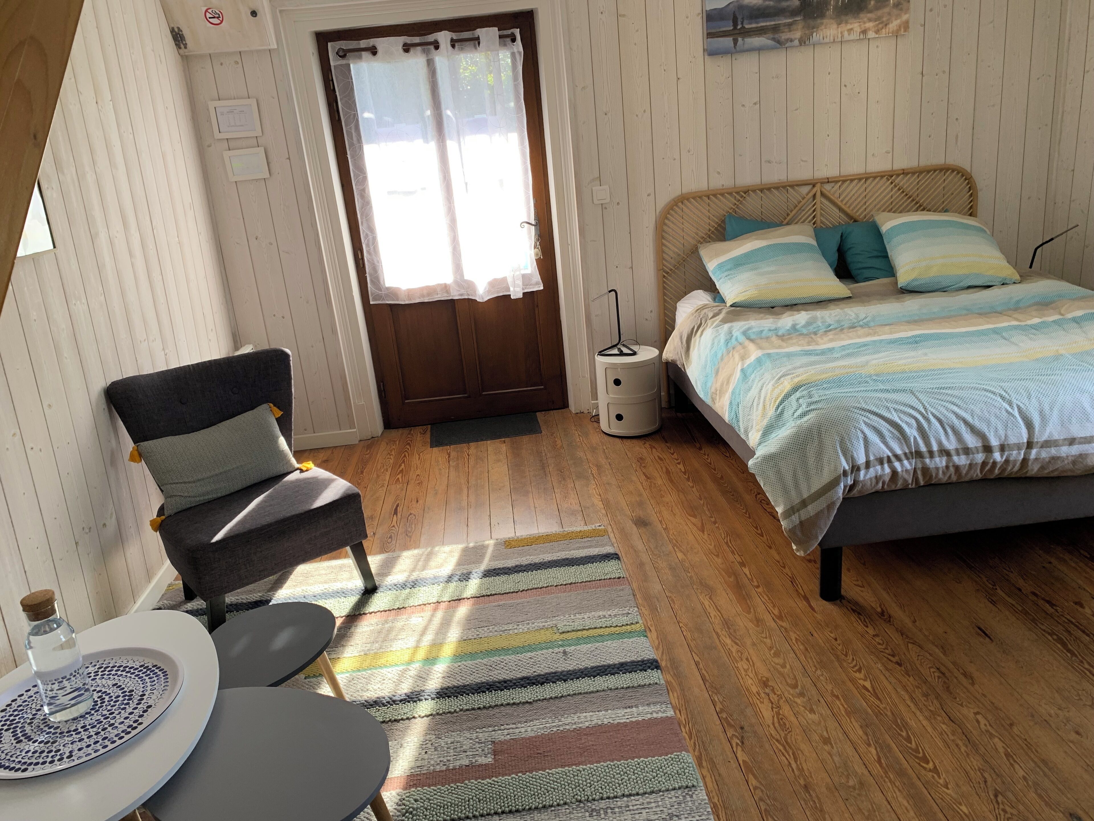 Una stanza con un letto, una sedia, un tavolino e una porta con tenda.
