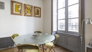 Un coin repas comprenant une table ronde en verre, quatre chaises et trois œuvres d’art encadrées accrochées au mur.