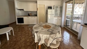 A compact kitchen with white cabinets, a microwave, and a refrigerator. There's a dining table with chairs and a patterned tablecloth. - Holiday rental, 2-bedroom apartment for 4 people, on the port of Hyères (HYERES PLAGE)