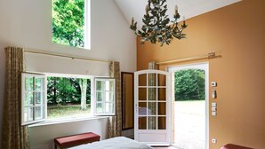 A bedroom with a bed, a bench, a window with curtains, a chandelier, and a door leading outside. - Manoir de Contres (Le Controis en Sologne)
