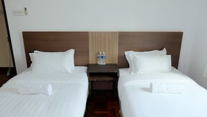 A hotel room with two beds, white linens, a wooden headboard, a nightstand with two water bottles, and a small wooden table. - Natol Homestay - Sydney Batu Kawa MJC New Townships (Kuching)