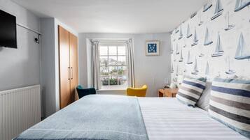 Une chambre d’hôtel avec un lit, une fenêtre avec des rideaux, une chaise, une petite table et un téléviseur fixé au mur.