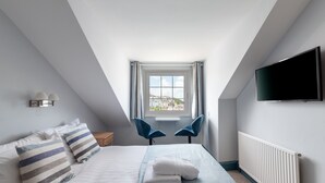 Un dormitorio con cama, almohadas, un televisor, una ventana y un radiador.