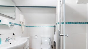 Un baño con lavamanos blanco, inodoro, cabina de ducha de vidrio y espejo.