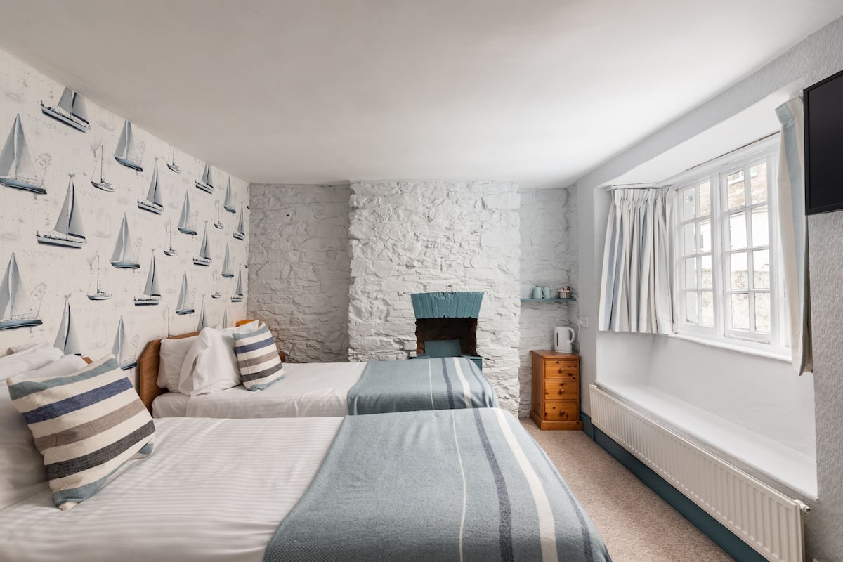 Un dormitorio con dos camas, una pared de piedra, una chimenea y una ventana con cortinas.