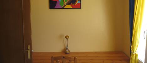 A room with a wooden desk, a chair, a door, and a colorful painting on the wall.