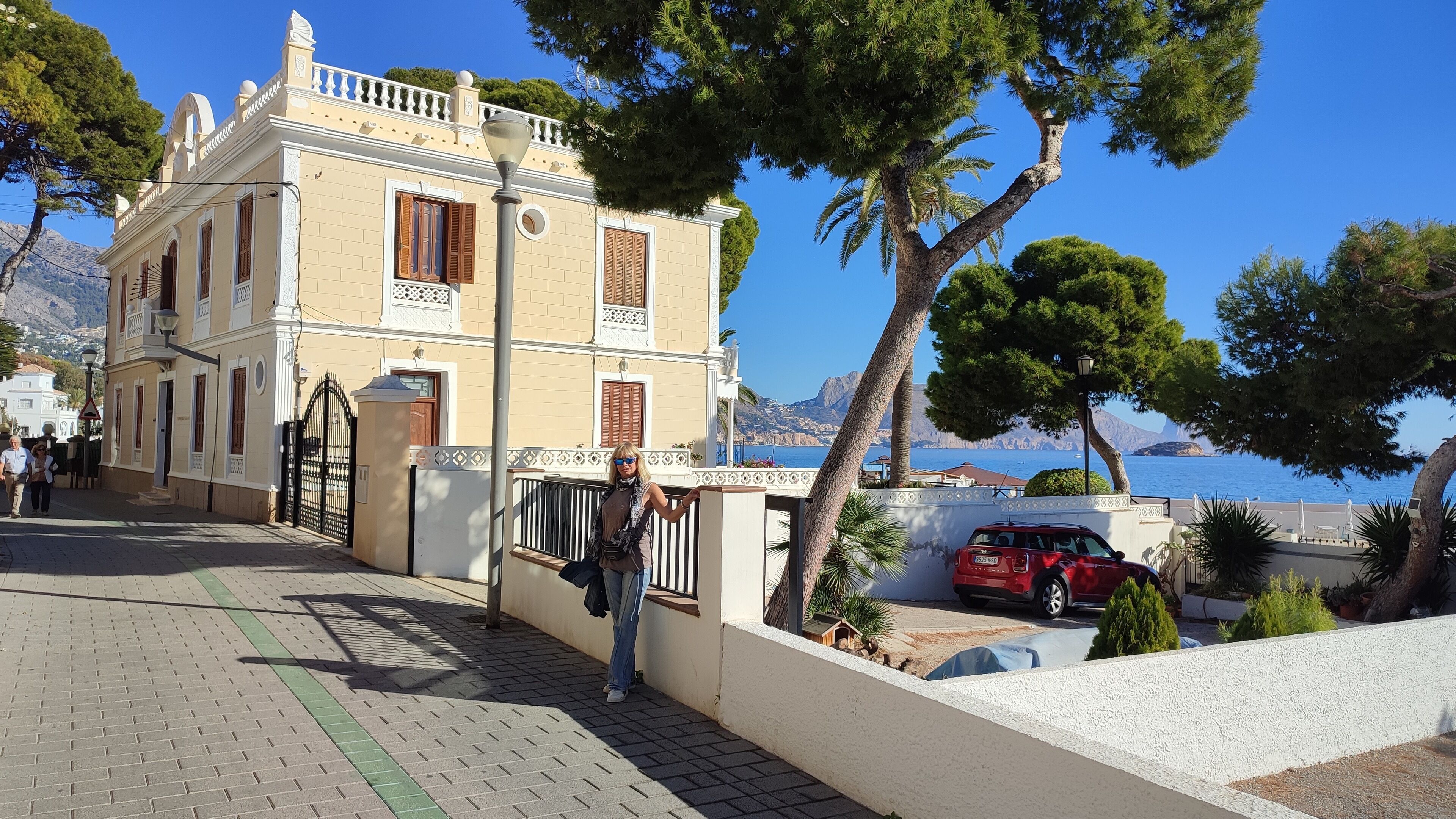 Un bâtiment situé sur la côte, doté d’une promenade dallée, d’une porte et d’une voiture rouge garée à proximité.