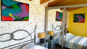 A bedroom with two beds, a brick wall, and colorful artwork. - APARTMENT NEW EXCEPTIONAL VIEW ON A COLINNE FACING THE SEA (a swimming pool) (benissa)