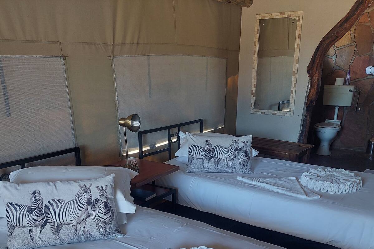 A hotel room with two beds, zebra-themed pillows, a wooden headboard, a mirror, and a bathroom visible through an open door.