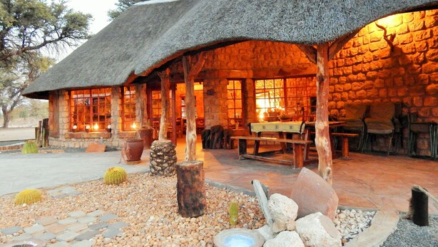 A rustic lodge with a thatched roof, stone walls, and a cozy interior with wooden furniture and a fireplace. - Torgos Lodge (Koes)