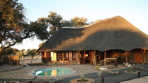 A thatched-roof building with a pool and outdoor seating area. - Torgos Lodge (Koes)