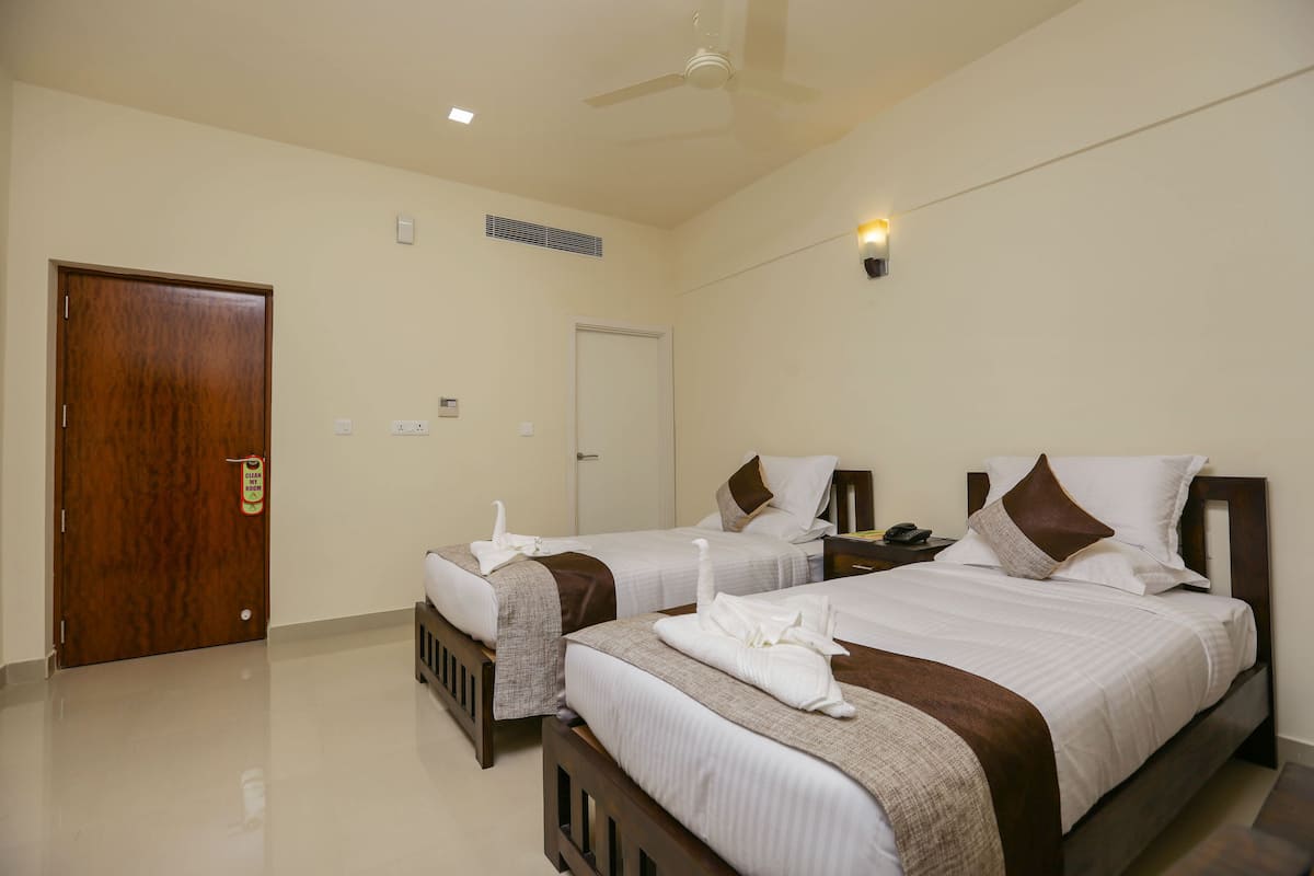 A hotel room with two beds, a ceiling fan, a door, and a light switch on the wall.