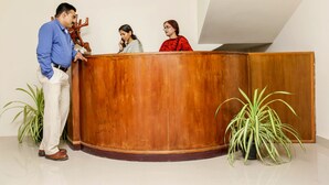 A reception area with a wooden desk, two potted plants, and three individuals standing around it. - Le Noor (Kanayannur)