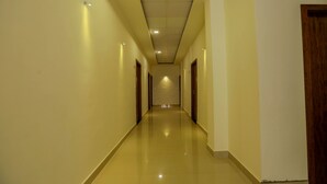A long, narrow hallway with doors on both sides, leading to a bright room at the end. - Le Noor (Kanayannur)