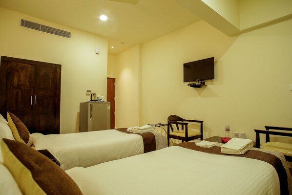 A hotel room with two beds, a TV mounted on the wall, a desk with a chair, and a refrigerator.