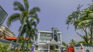A hotel with a modern facade, a prominent entrance, and a parking area with cars. - Le Noor (Kanayannur)