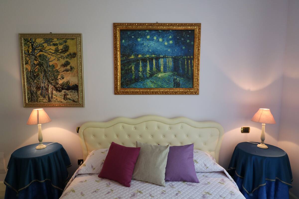 A bedroom with a bed, two bedside tables, two lamps, and two framed artworks on the wall.