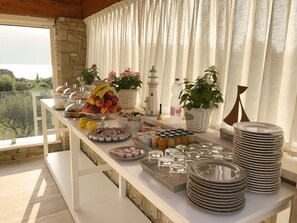 A buffet table with various food items, including fruits, pastries, and beverages, set against a backdrop of a scenic view. - La cascata negli ulivi (Toscolano Maderno)