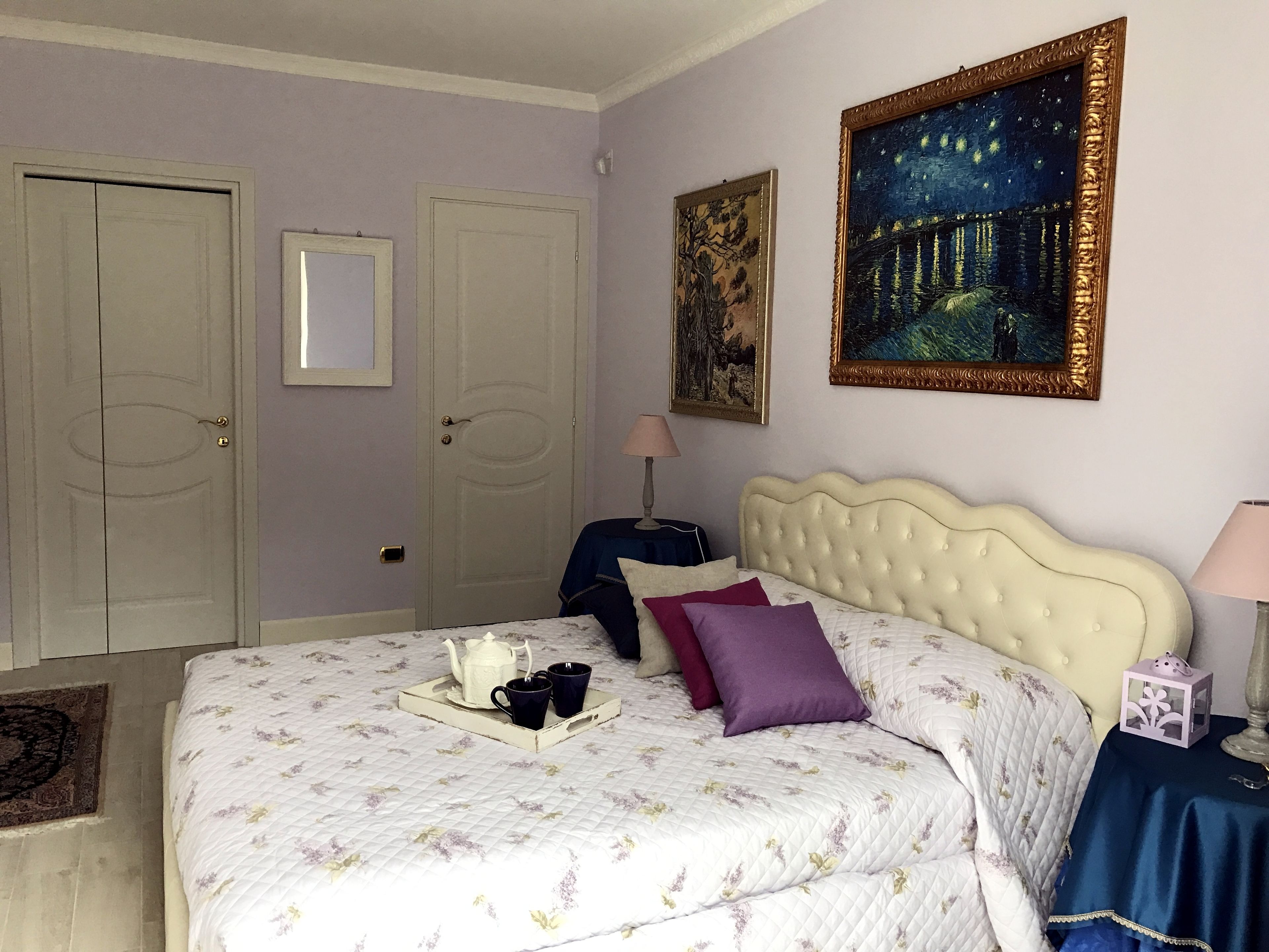 Een slaapkamer met een bed, nachtkastje, kapstok en een schilderij aan de muur.