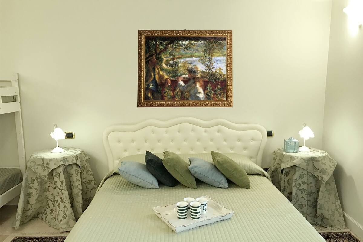 A neatly arranged bedroom with a white bed, a framed painting above, and bedside tables with lamps.