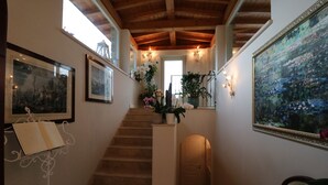 A staircase with a wooden ceiling, framed artwork on the walls, and a potted plant at the top. - La cascata negli ulivi (Toscolano Maderno)