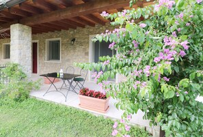 A stone building with a covered patio, a table and chairs, and a planter with flowers. - La cascata negli ulivi (Toscolano Maderno)