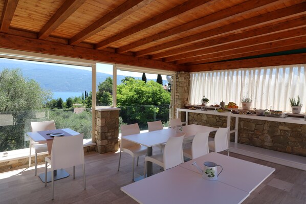 A dining area with white furniture, a stone wall, and a view of the lake. - La cascata negli ulivi (Toscolano Maderno)
