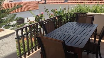 Una terraza con mesa y sillas, barandilla y vista a un edificio de tejado rojo.