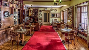Un comedor tradicional con muebles de madera, alfombra roja y una variedad de relojes y objetos decorativos en las paredes.