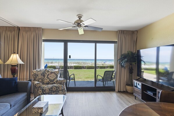 Una sala de estar con sofá, sillón y televisor, con vista a la playa.