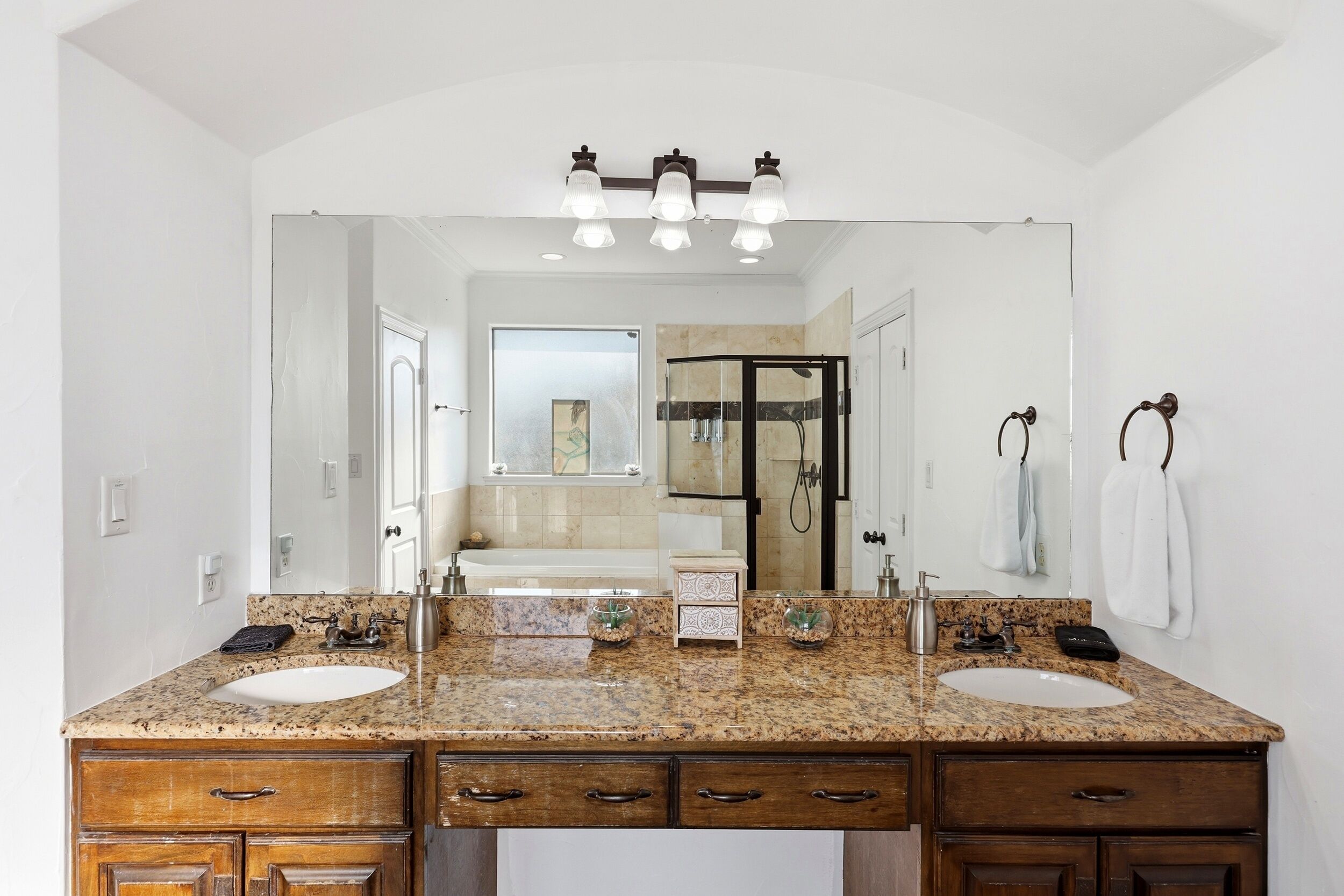 A bathroom with a double sink vanity, a large mirror, and a shower area visible through the glass door.
