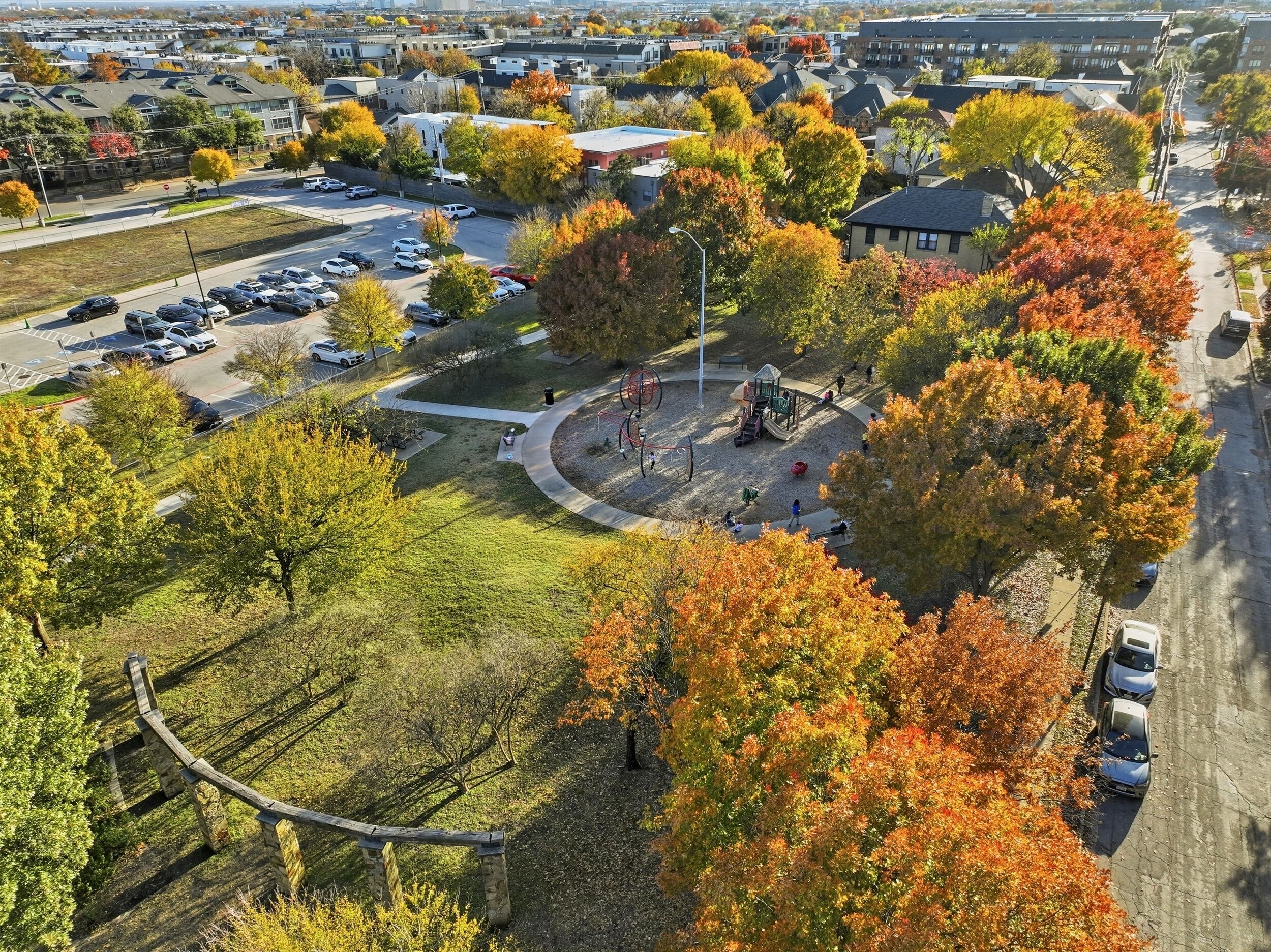 An aerial view of a residential area with a playground, parking lot, and autumn foliage.