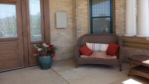 A corner of a building with a wooden door, a wicker sofa with red cushions, a potted plant, and a brick wall. - Charming & Historic Babs Condo on Hip Strip- Missoula's Best! (Missoula)