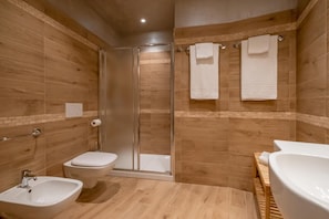 A modern bathroom with wooden walls, a glass shower enclosure, a toilet, a bidet, and a sink. - Le Camere di Nanà (Sanremo)