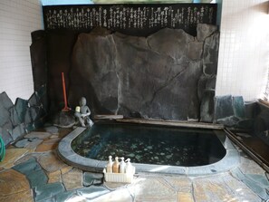 A stone-tiled pool area with a large rock wall, a statue, and a row of toiletries. - Seisenso (Nozawaonsen)
