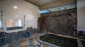 Une salle de bain au sol carrelé, avec un mur en pierre, une petite piscine et une fenêtre.
