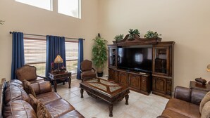 A spacious living room with a leather sofa, a coffee table, a television, and a cabinet. - Spacious Family Retreat | Pool Access & Beach Nearby (Corpus Christi)